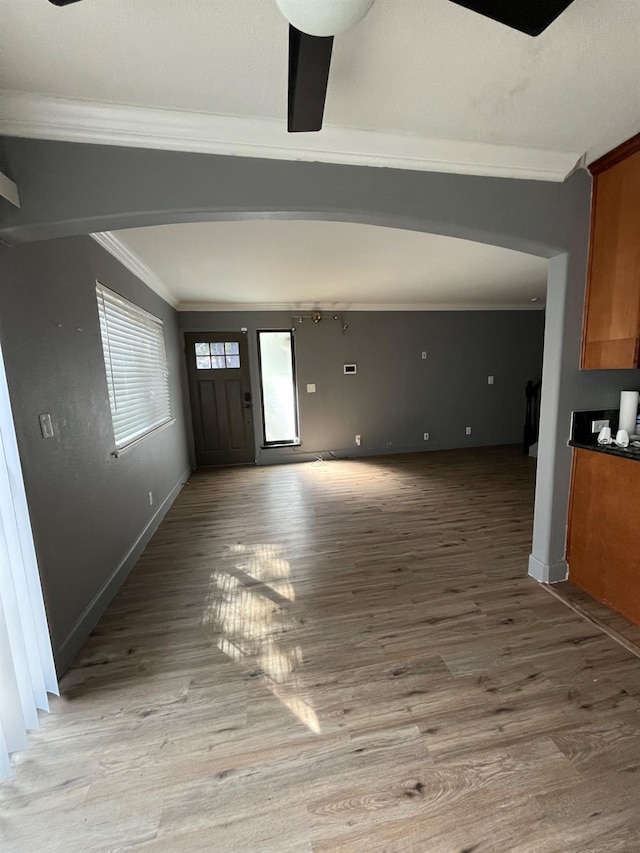 interior space with light wood finished floors, ornamental molding, arched walkways, and baseboards