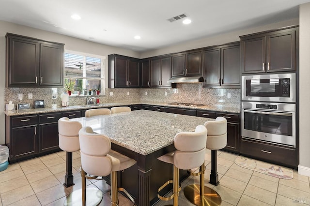 kitchen featuring decorative backsplash, a kitchen island, a breakfast bar, and light stone countertops