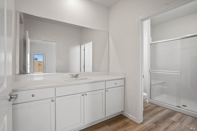 bathroom with hardwood / wood-style flooring, toilet, vanity, and a shower with door