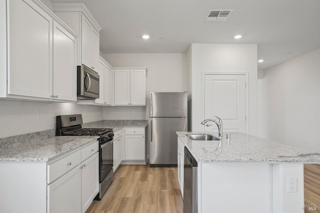 kitchen featuring sink, a kitchen island with sink, appliances with stainless steel finishes, white cabinets, and light stone counters