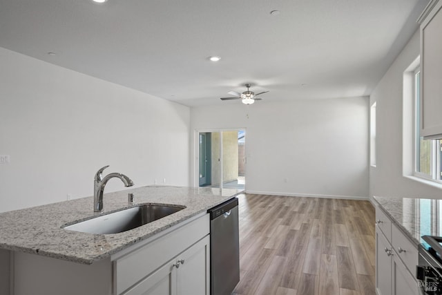 kitchen with light stone countertops, sink, dishwasher, and an island with sink