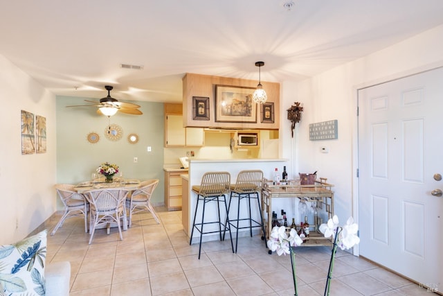 kitchen with ceiling fan, hanging light fixtures, white microwave, kitchen peninsula, and light tile patterned floors