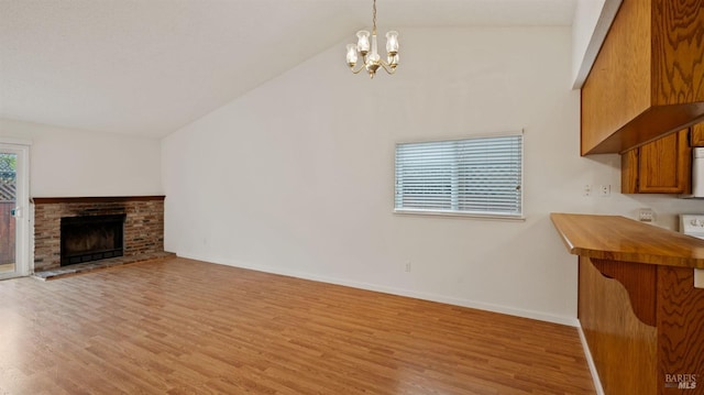 living room featuring a notable chandelier, vaulted ceiling, a brick fireplace, and light wood-type flooring