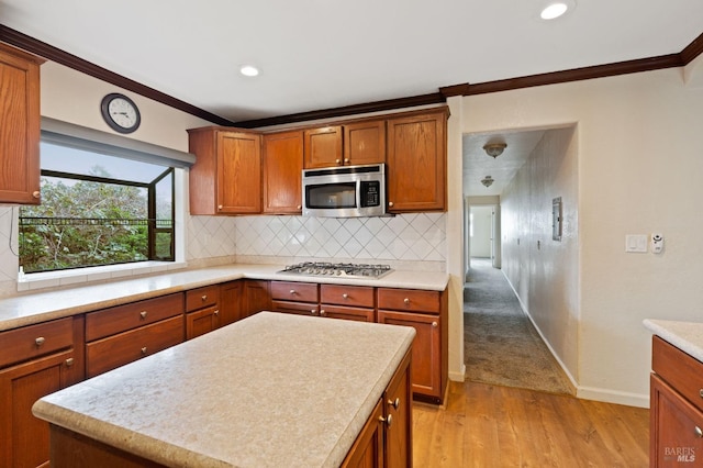 kitchen featuring light wood-type flooring, crown molding, tasteful backsplash, a kitchen island, and appliances with stainless steel finishes