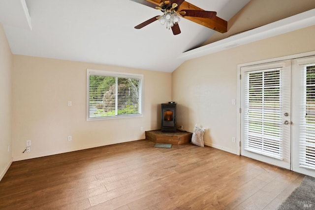 unfurnished living room with ceiling fan, a wood stove, lofted ceiling with beams, and wood-type flooring