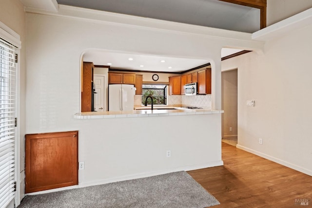 kitchen featuring white refrigerator, hardwood / wood-style floors, kitchen peninsula, tasteful backsplash, and ornamental molding