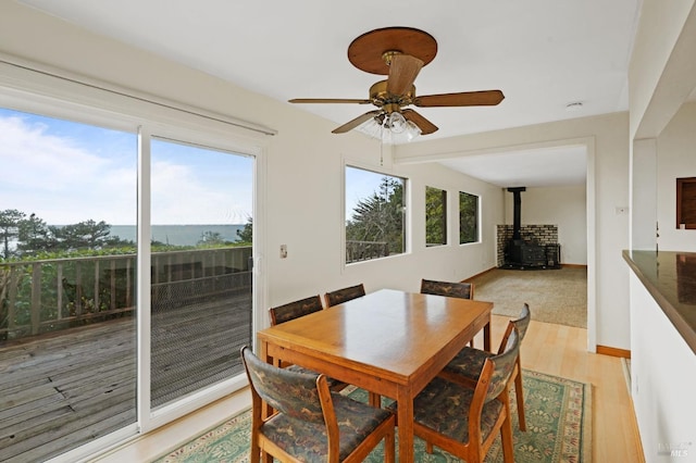 dining space with a wood stove, light hardwood / wood-style flooring, ceiling fan, and a water view