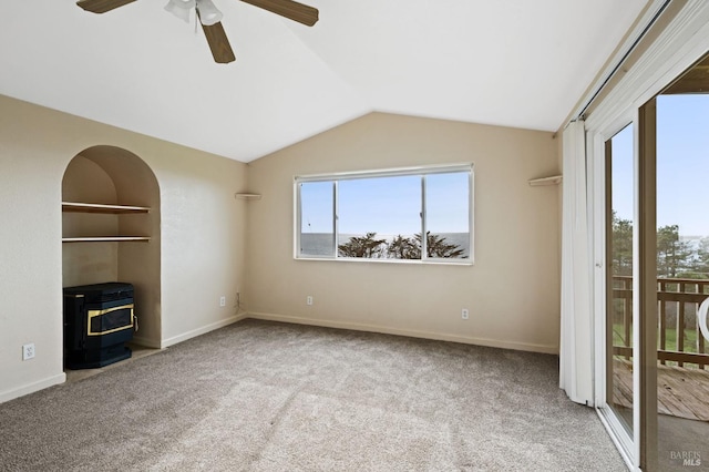 unfurnished living room featuring ceiling fan, a wealth of natural light, a wood stove, and light carpet