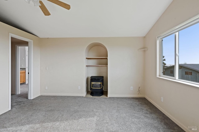 carpeted empty room featuring a wood stove, ceiling fan, and vaulted ceiling