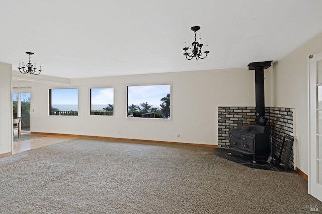 unfurnished living room featuring an inviting chandelier, a wood stove, and carpet flooring