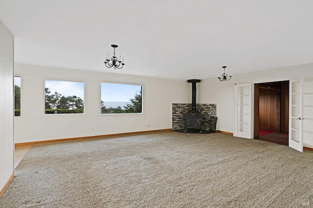 unfurnished living room featuring a notable chandelier, a wood stove, and carpet floors