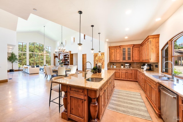 kitchen featuring sink, light stone counters, a center island with sink, decorative light fixtures, and stainless steel dishwasher