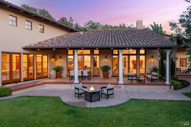 back house at dusk with a patio, a fire pit, and a lawn