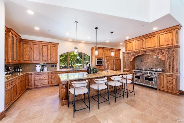 kitchen with a kitchen bar, light stone counters, decorative light fixtures, stainless steel appliances, and a kitchen island with sink