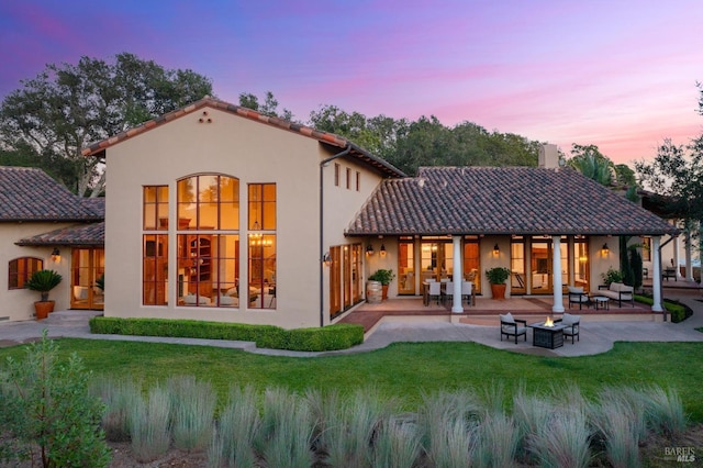 back house at dusk with an outdoor living space, a yard, and a patio area