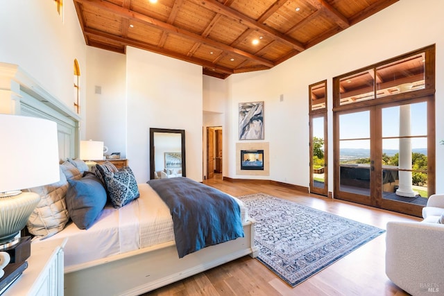 bedroom with wood ceiling, a multi sided fireplace, access to outside, beamed ceiling, and light wood-type flooring