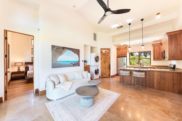 living room featuring stacked washer / drying machine, a towering ceiling, sink, and ceiling fan