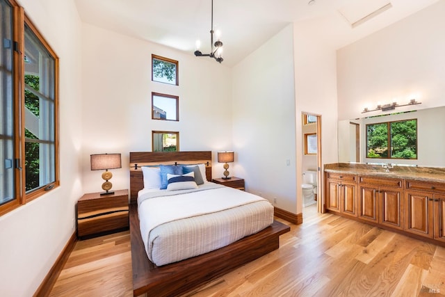 bedroom with a towering ceiling, ensuite bath, sink, and light hardwood / wood-style flooring