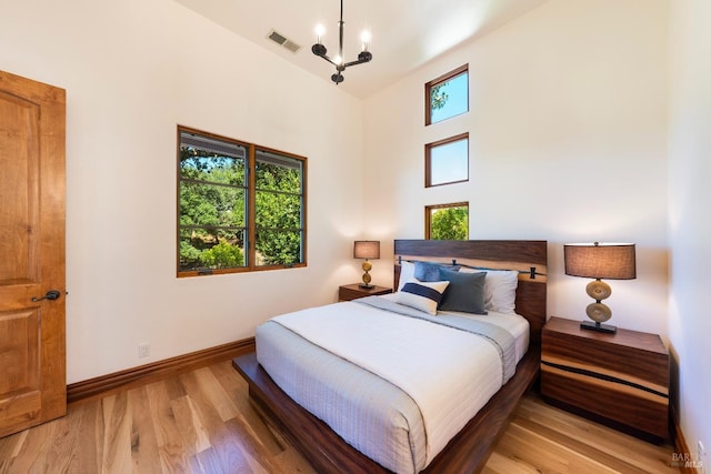 bedroom featuring multiple windows, a notable chandelier, light hardwood / wood-style flooring, and a high ceiling