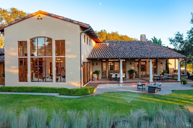 rear view of property featuring a patio, a yard, and a fire pit