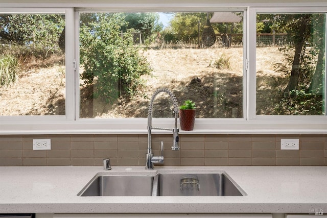 kitchen featuring light stone countertops, tasteful backsplash, and sink