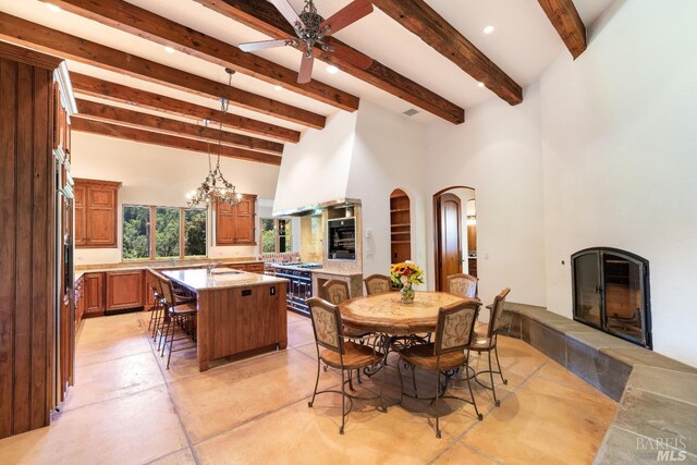 dining space with light tile patterned flooring, ceiling fan with notable chandelier, a tile fireplace, and beamed ceiling