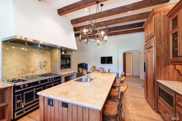 kitchen with built in appliances, premium range hood, tasteful backsplash, a kitchen island with sink, and light tile patterned floors