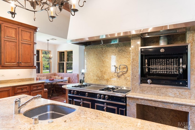 kitchen with wall chimney range hood, sink, a notable chandelier, and light stone countertops