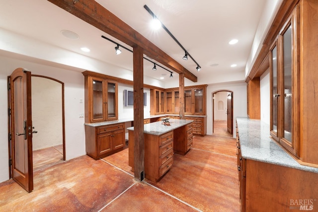 kitchen with beam ceiling, french doors, light stone countertops, and a kitchen island