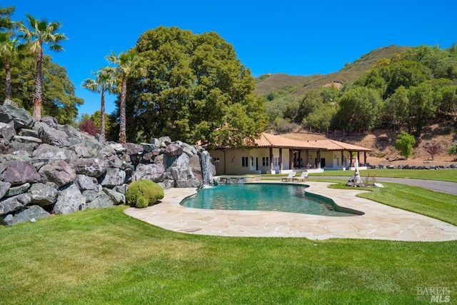 view of pool with a patio area, pool water feature, a lawn, and a mountain view