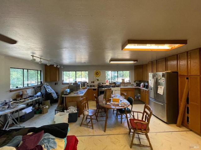 kitchen with brown cabinets, stainless steel appliances, rail lighting, light countertops, and a textured ceiling