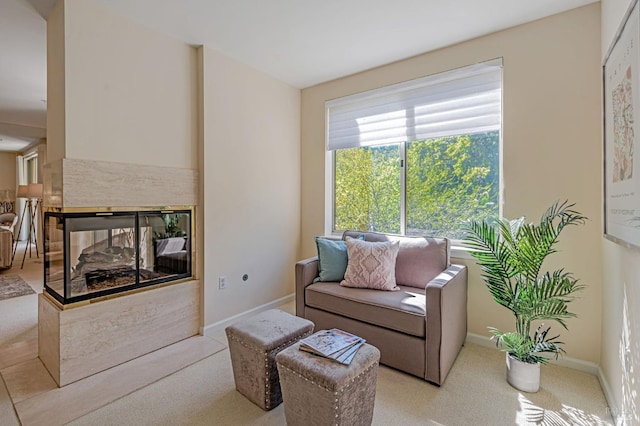 carpeted living room featuring a multi sided fireplace and baseboards