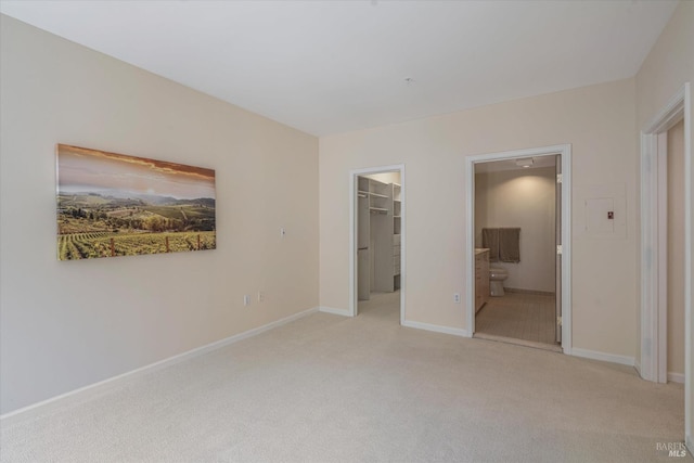 unfurnished bedroom featuring light colored carpet, ensuite bath, a walk in closet, and a closet