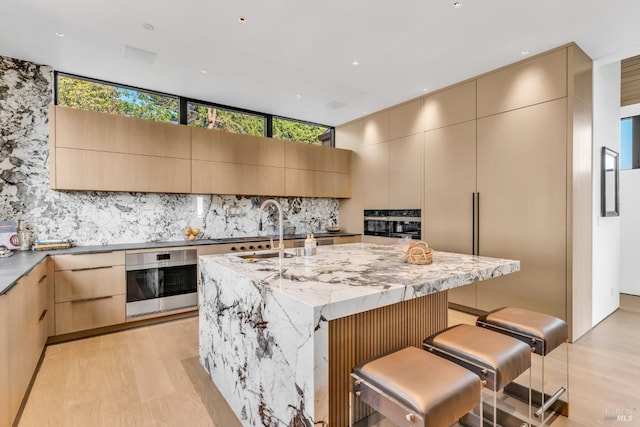 kitchen with oven, a kitchen bar, decorative backsplash, a kitchen island with sink, and light stone countertops