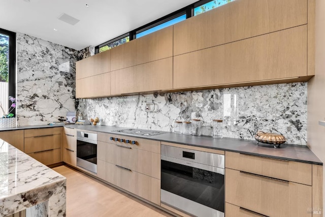 kitchen featuring appliances with stainless steel finishes, backsplash, light brown cabinetry, and light hardwood / wood-style flooring