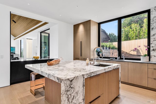 kitchen with light stone counters, sink, a kitchen island with sink, and light hardwood / wood-style flooring