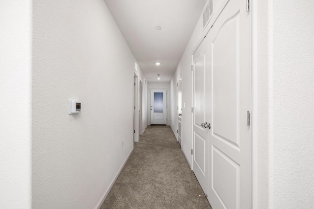 hallway featuring light colored carpet, visible vents, and baseboards