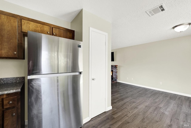 kitchen featuring dark hardwood / wood-style flooring, a fireplace, stainless steel fridge, and a textured ceiling