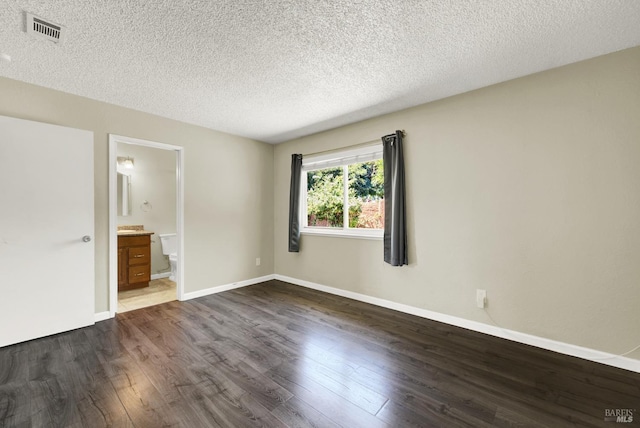 unfurnished bedroom with ensuite bathroom, a textured ceiling, and dark hardwood / wood-style flooring