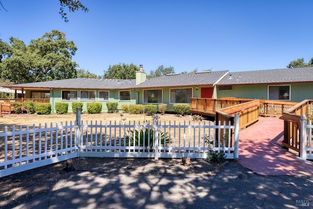 ranch-style house with a fenced front yard, a chimney, and a wooden deck