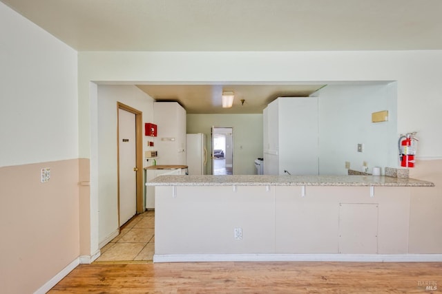 kitchen featuring light wood-type flooring, freestanding refrigerator, white cabinetry, and a peninsula