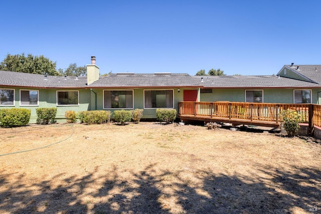 back of house with a deck, a chimney, and stucco siding