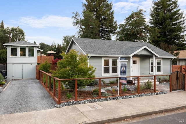 view of front of property featuring a fenced front yard, a gate, a shingled roof, and gravel driveway