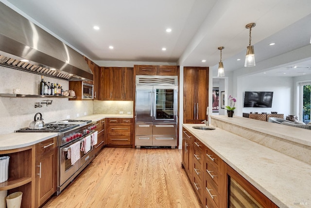 kitchen with light stone counters, decorative light fixtures, backsplash, built in appliances, and light wood-type flooring