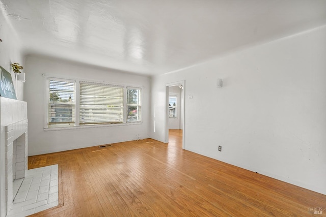 unfurnished living room with light hardwood / wood-style floors and a brick fireplace