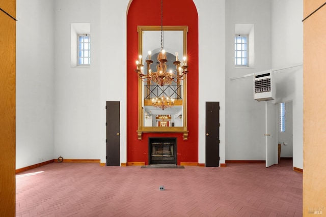 unfurnished living room featuring a wealth of natural light, baseboards, a notable chandelier, and a towering ceiling