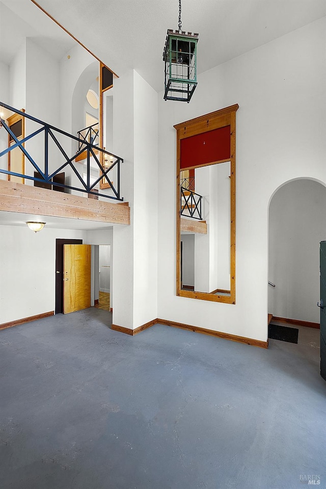 unfurnished living room featuring arched walkways, baseboards, concrete floors, and a high ceiling