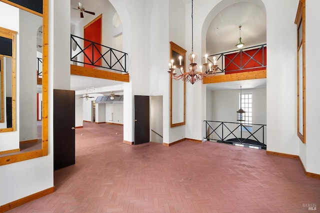 interior space with ceiling fan with notable chandelier, a high ceiling, and baseboards