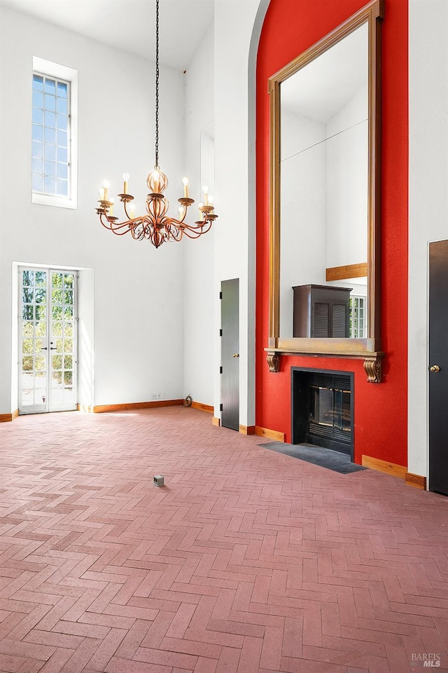 unfurnished living room featuring baseboards, a fireplace with flush hearth, brick floor, a towering ceiling, and a chandelier