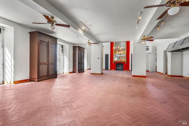 unfurnished living room featuring track lighting, baseboards, beamed ceiling, ceiling fan with notable chandelier, and a glass covered fireplace